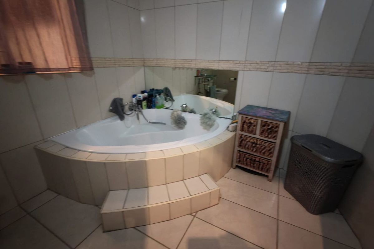 A bathroom featuring a corner bathtub with tiled surround, wall-mounted mirror, and neutral floor tiling.