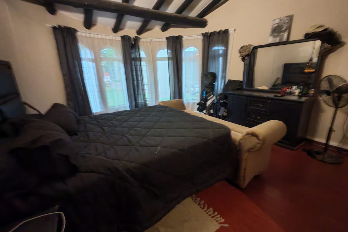 Spacious bedroom featuring exposed timber ceiling beams, a large bay window, and hardwood flooring.