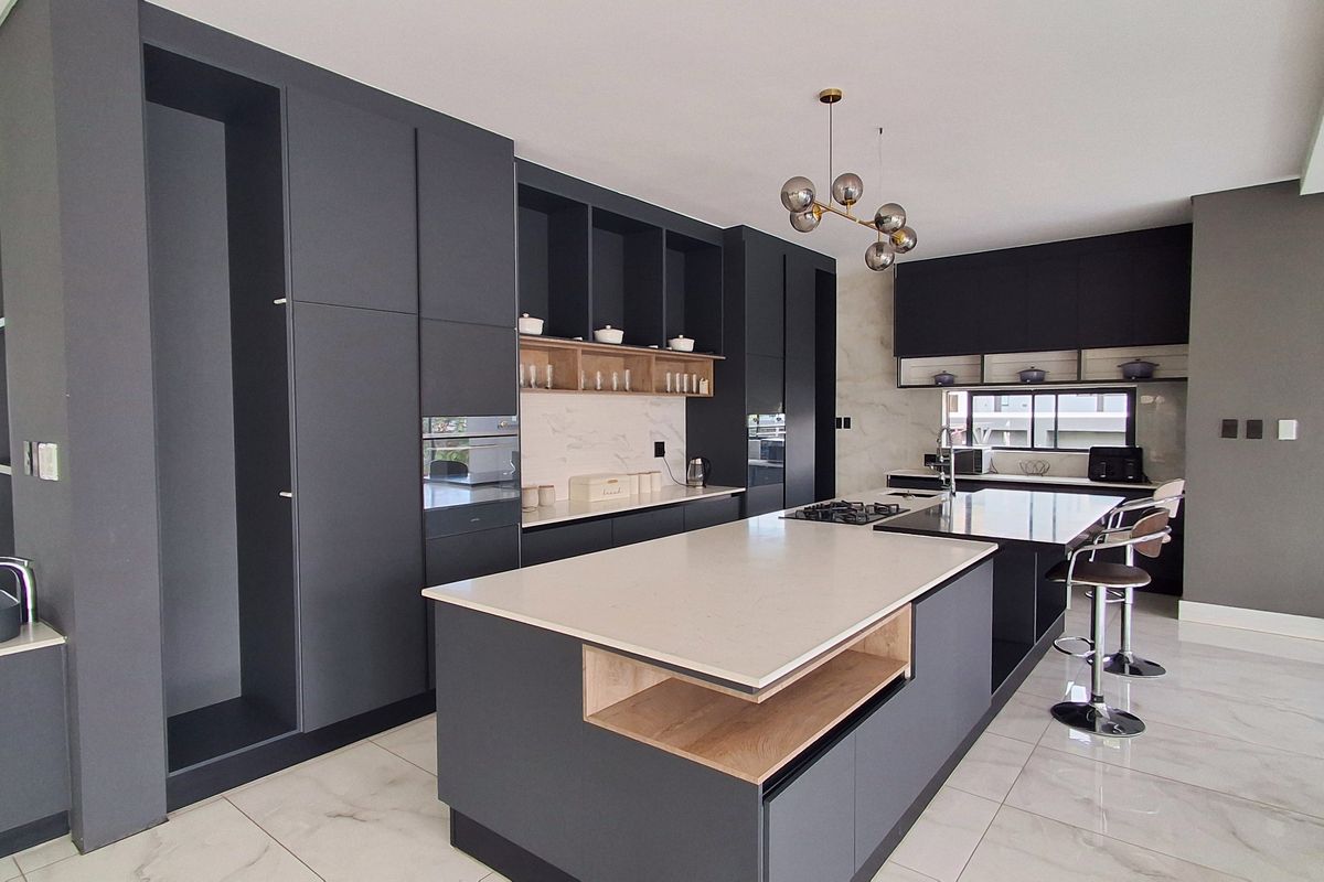 Modern kitchen featuring dark matte cabinetry, a large central island with stone countertops, integrated appliances, and high-end marble-look finishes.