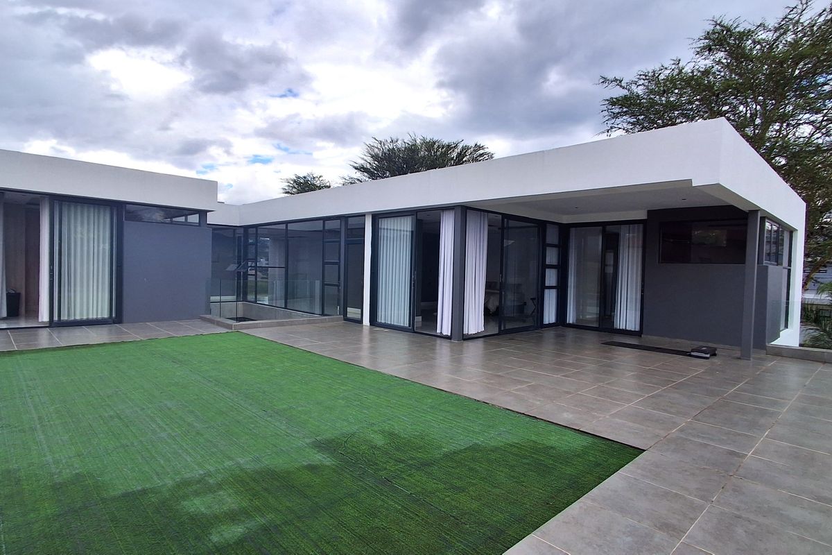 Modern rear exterior featuring a spacious tiled patio, extensive sliding glass doors, and a well-maintained artificial grass lawn.