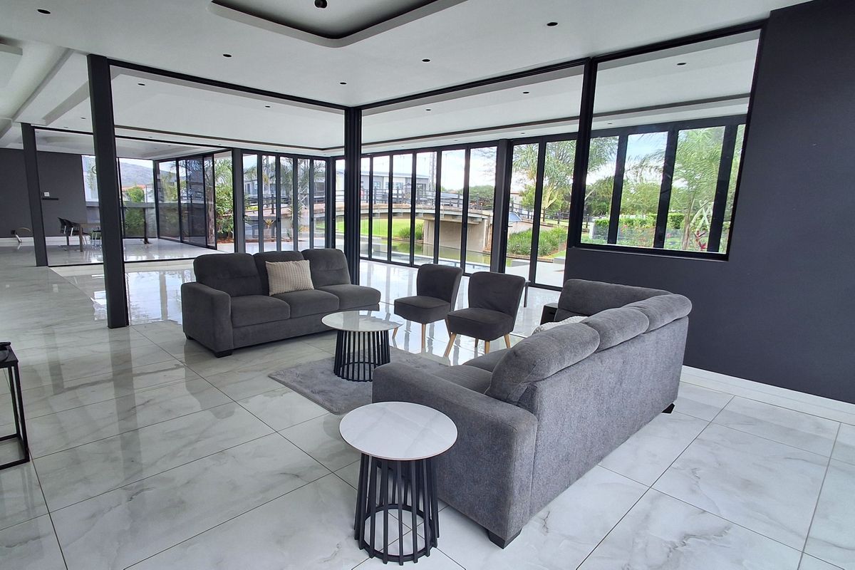 Spacious modern living area featuring large format floor tiles, extensive floor-to-ceiling black aluminium windows, and sophisticated recessed ceiling lighting with a contemporary open-plan design.