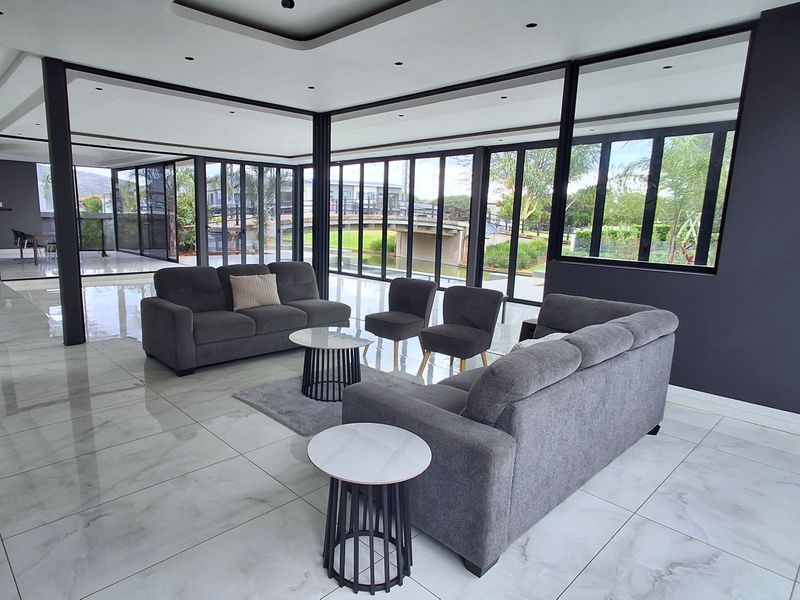 Spacious modern living area featuring large format floor tiles, extensive floor-to-ceiling black aluminium windows, and sophisticated recessed ceiling lighting with a contemporary open-plan design.