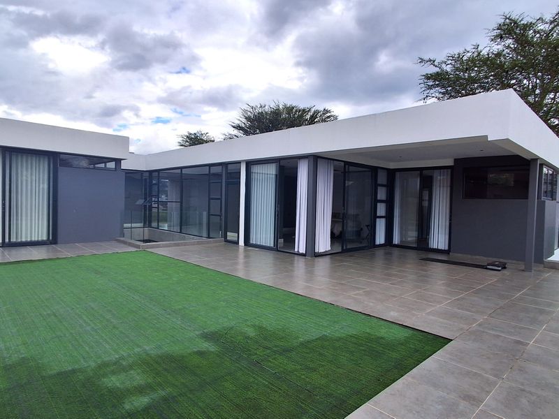 Modern rear exterior featuring a spacious tiled patio, extensive sliding glass doors, and a well-maintained artificial grass lawn.