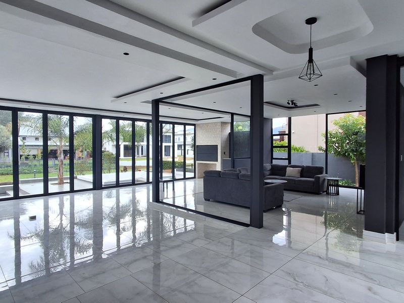 Spacious open-plan living area featuring large format polished tiles, modern recessed ceiling details, and extensive floor-to-ceiling glass folding doors opening to the garden.