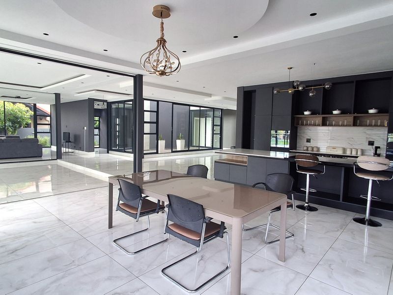 Spacious open-plan living and kitchen area featuring modern dark cabinetry, a large kitchen island, marble-look flooring, and expansive sliding glass doors.