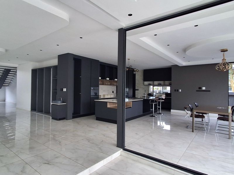 Modern open-plan living area featuring a sleek kitchen with a central island, high-gloss floor tiles, and expansive glass doors leading to the exterior.