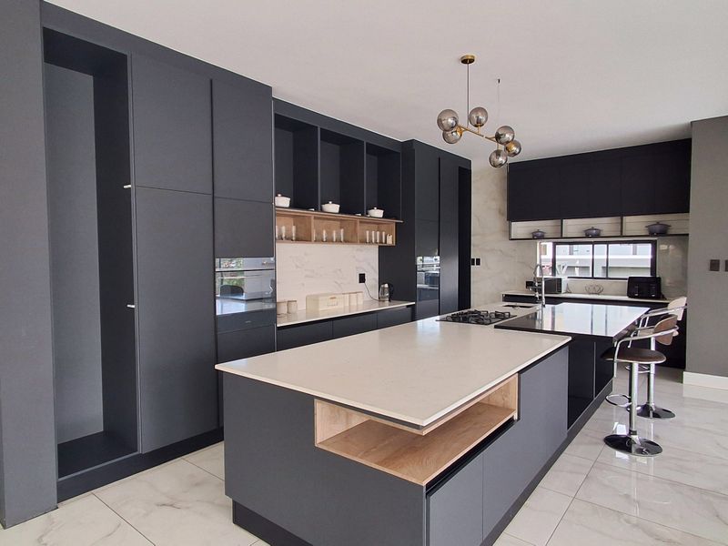 Modern kitchen featuring dark matte cabinetry, a large central island with stone countertops, integrated appliances, and high-end marble-look finishes.