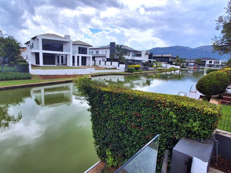 A scenic view of a residential canal estate featuring modern architectural homes, manicured landscaping, and calm water frontage.