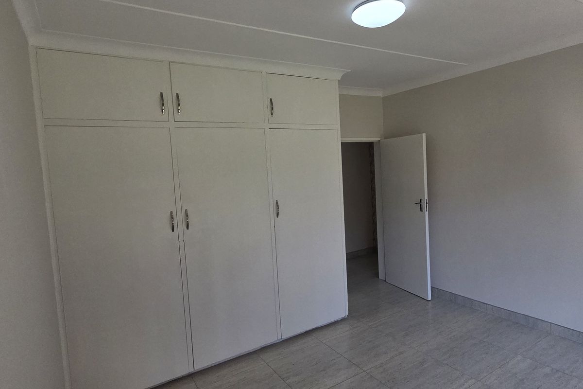 A clean, empty bedroom featuring built-in cupboards, tiled flooring, and neutral wall finishes, providing a versatile space ready for personalization.