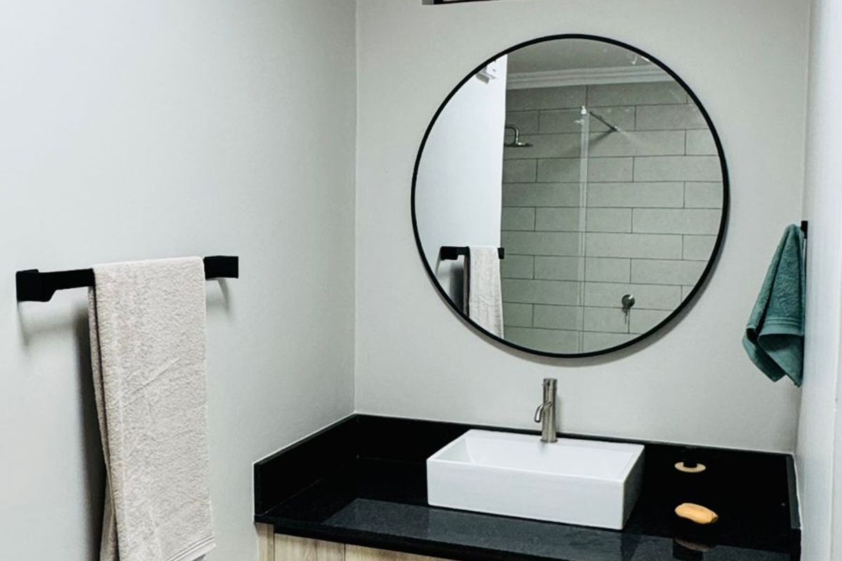 Modern bathroom featuring a floating vanity with a black stone countertop, vessel sink, circular mirror, and tiled flooring.