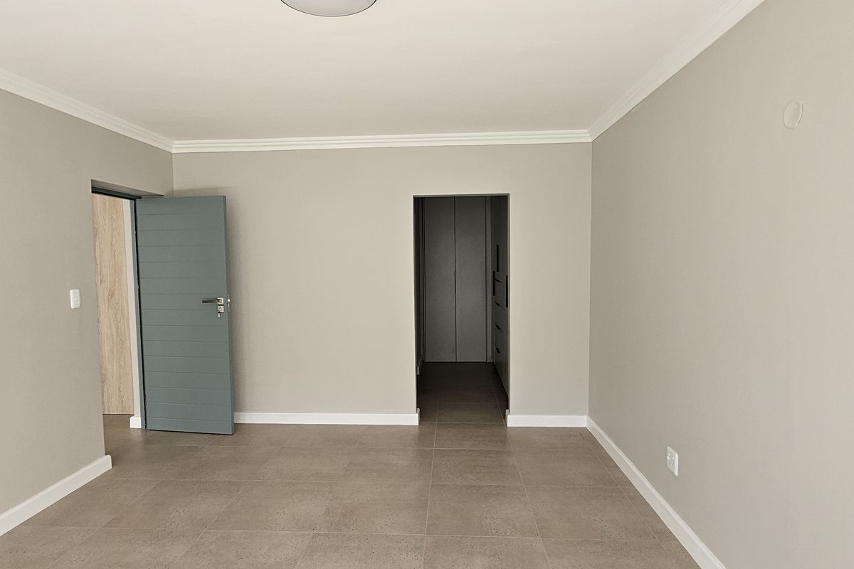 A bright, empty bedroom featuring neutral wall paint, tiled flooring, crown molding, and a modern grey interior door leading to a walk-in closet area.