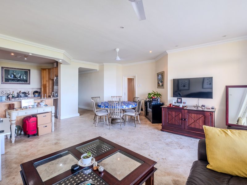 Spacious open-plan living and dining area featuring stone tile flooring, crown molding, and an integrated kitchen space.