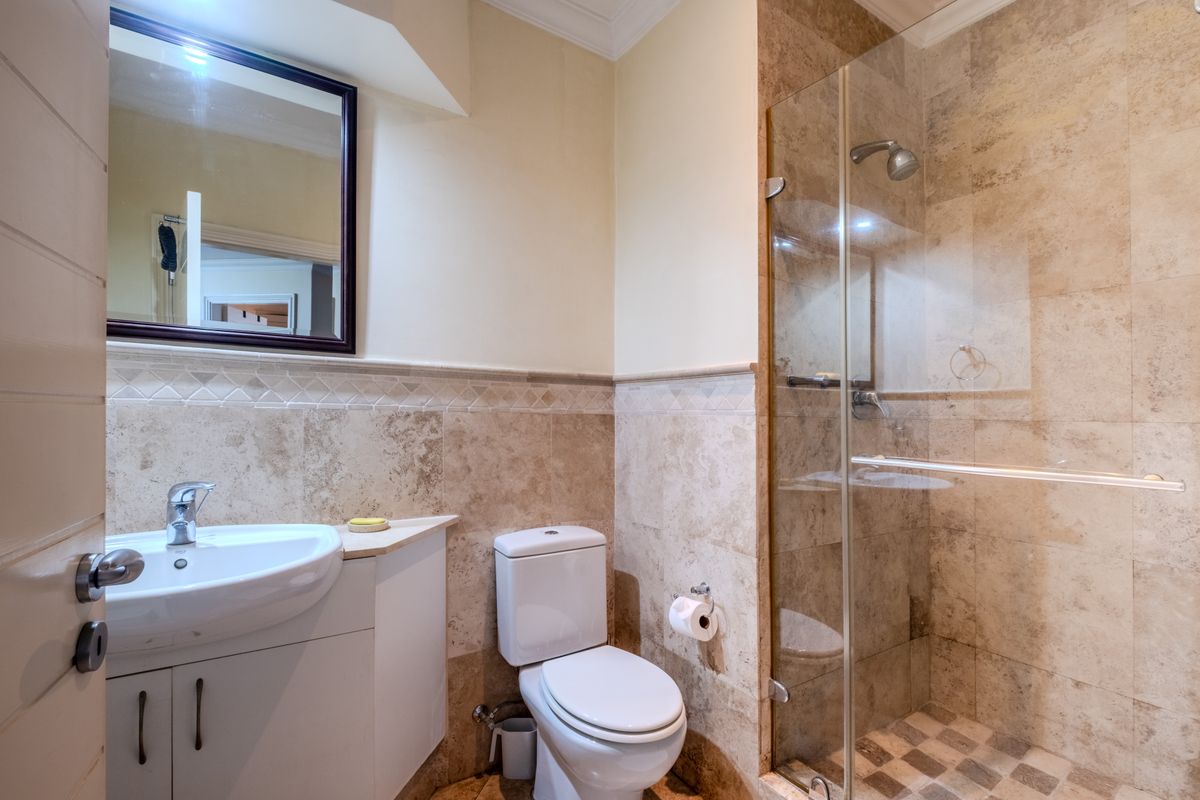 A well-maintained bathroom featuring a vanity cabinet with a ceramic basin, a glass-enclosed shower, and neutral travertine wall and floor tiling.