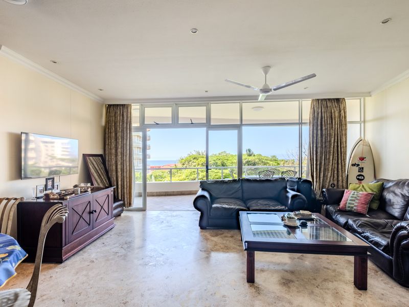 Spacious living room featuring stone flooring, recessed lighting, and large sliding glass doors that open onto a balcony with scenic views.