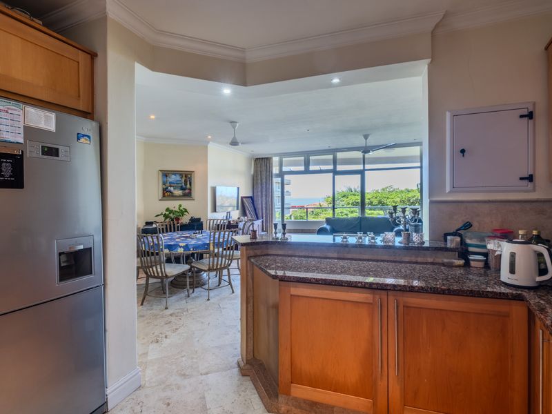 Open-plan kitchen and living area featuring granite countertops, wooden cabinetry, stone flooring, and large sliding doors leading to a balcony with scenic views.