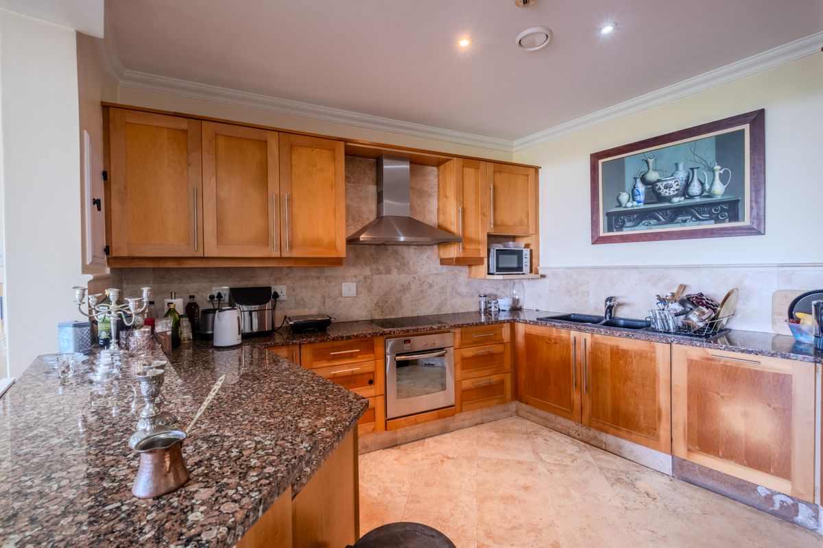 A functional kitchen featuring wooden cabinetry, granite countertops, stone tile backsplash, and integrated stainless steel appliances, including an oven and extractor fan.