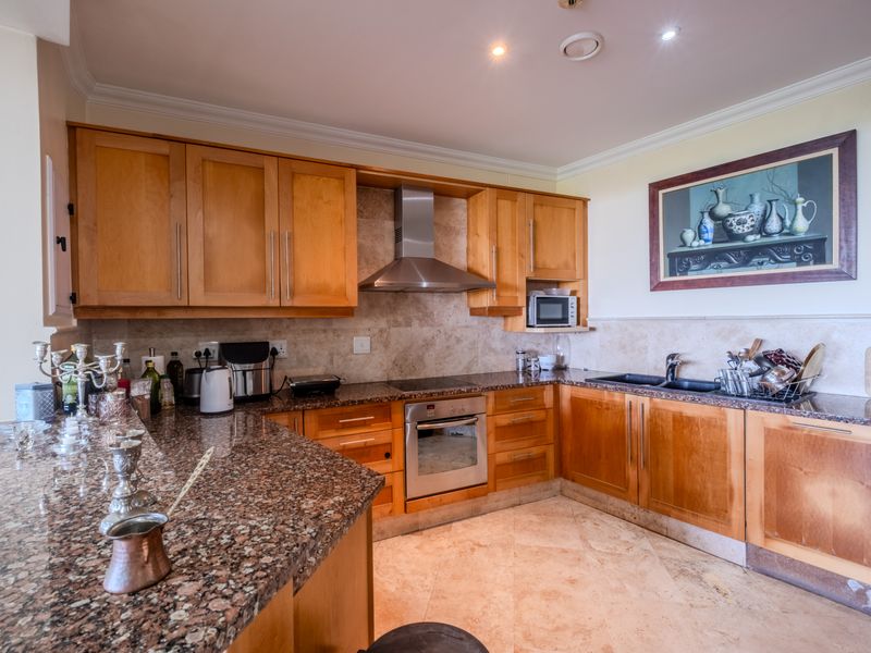 A functional kitchen featuring wooden cabinetry, granite countertops, stone tile backsplash, and integrated stainless steel appliances, including an oven and extractor fan.