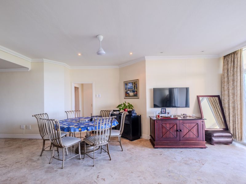 A spacious living and dining area featuring neutral stone tile flooring, crown molding, and access to an outdoor balcony through a sliding glass door.