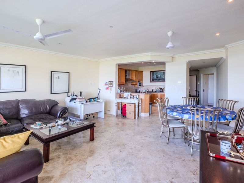 Spacious open-plan living and dining area featuring stone tile flooring, ceiling fans, and an integrated kitchen with wooden cabinetry.
