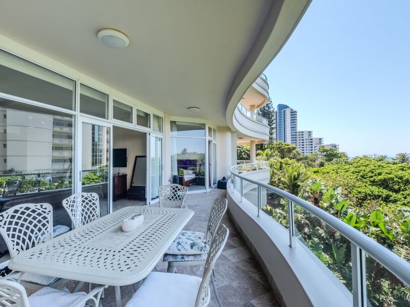 Spacious curved balcony featuring tiled flooring, a glass balustrade, and direct access to the interior living areas through large sliding glass doors.