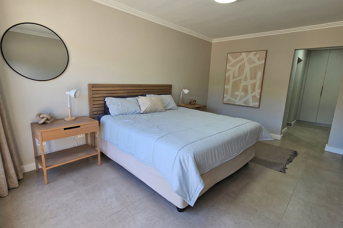 A well-maintained bedroom featuring neutral wall tones, tiled flooring, and built-in cupboards in the adjacent hallway area.