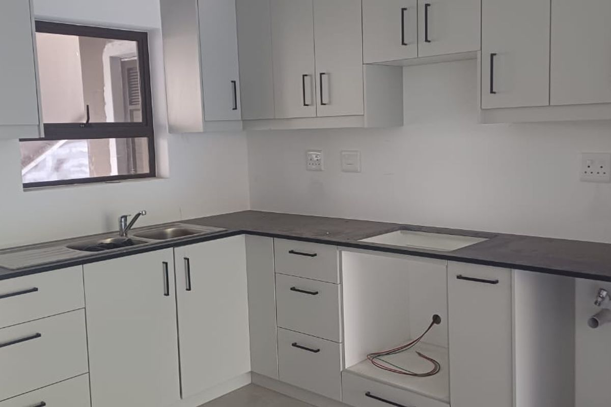 A clean, modern kitchen featuring light grey cabinetry, dark countertops, and integrated plumbing connections, ready for appliance installation.