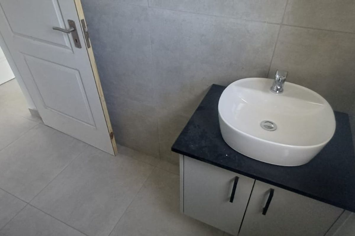 A modern bathroom featuring a vessel sink on a stone countertop vanity, with neutral wall and floor tiling and an unfinished door frame.