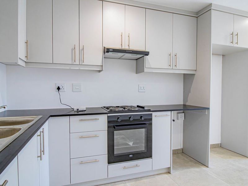 Modern kitchen featuring clean white cabinetry, dark countertops, built-in oven, gas hob, extractor fan, and a stainless steel double sink.
