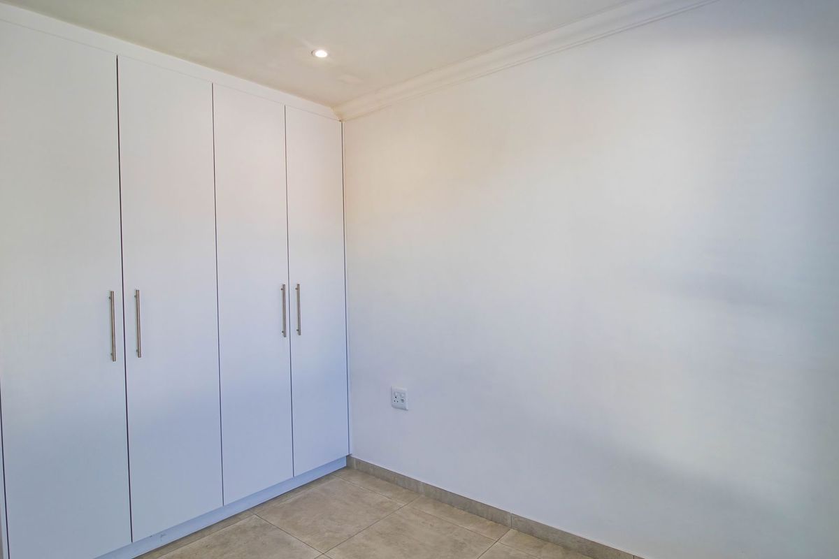 A clean, empty bedroom featuring neutral tiled flooring, white built-in cupboards, and recessed ceiling lighting, providing a blank canvas for personalization.