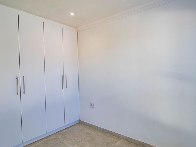 A clean, empty bedroom featuring neutral tiled flooring, white built-in cupboards, and recessed ceiling lighting, providing a blank canvas for personalization.