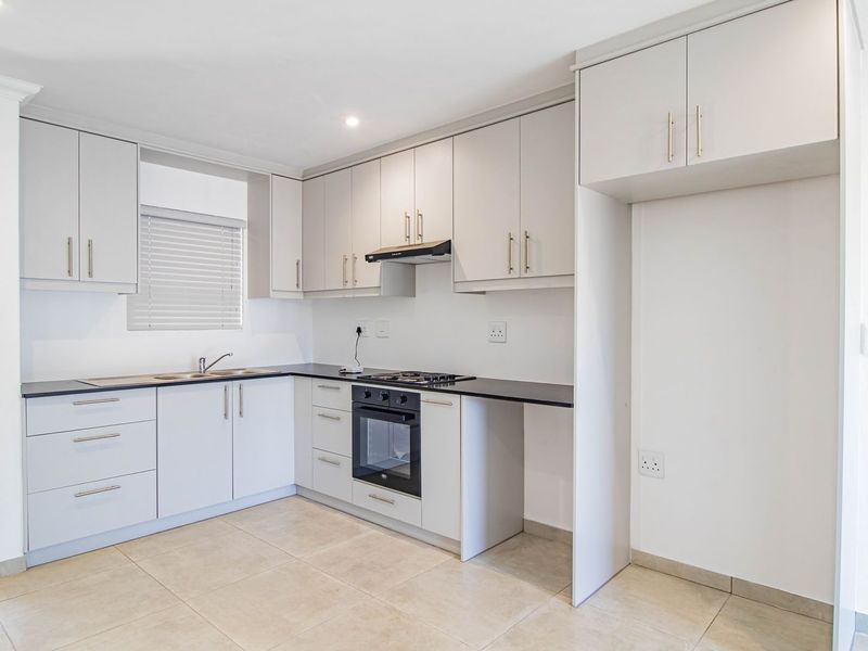 Modern kitchen featuring light grey cabinetry, dark countertops, built-in oven, gas hob, extractor fan, and tiled flooring with access to a balcony.