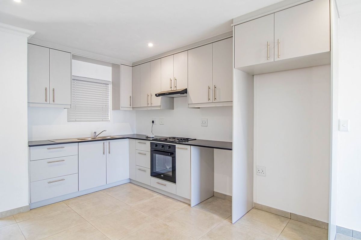 Modern kitchen featuring light grey cabinetry, dark countertops, built-in oven, gas hob, extractor fan, and tiled flooring with access to a balcony.
