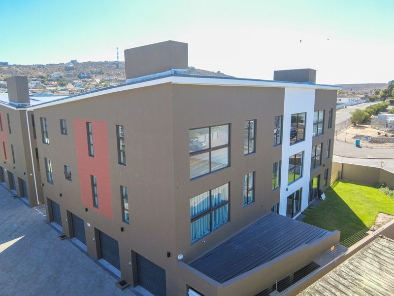 Aerial view of a modern multi-level apartment complex featuring a paved driveway, integrated garages, and landscaped lawn area.
