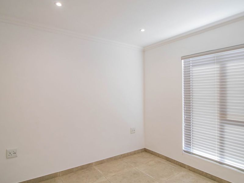 A clean, empty bedroom featuring neutral tiled flooring, recessed ceiling lighting, and fitted venetian blinds on the window.