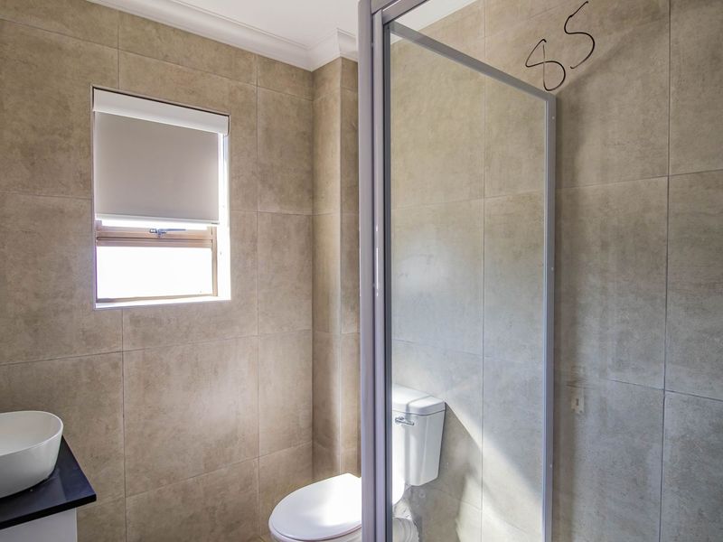 A modern bathroom featuring neutral wall tiles, a vessel sink with chrome faucet, a toilet, and a glass-enclosed shower area.
