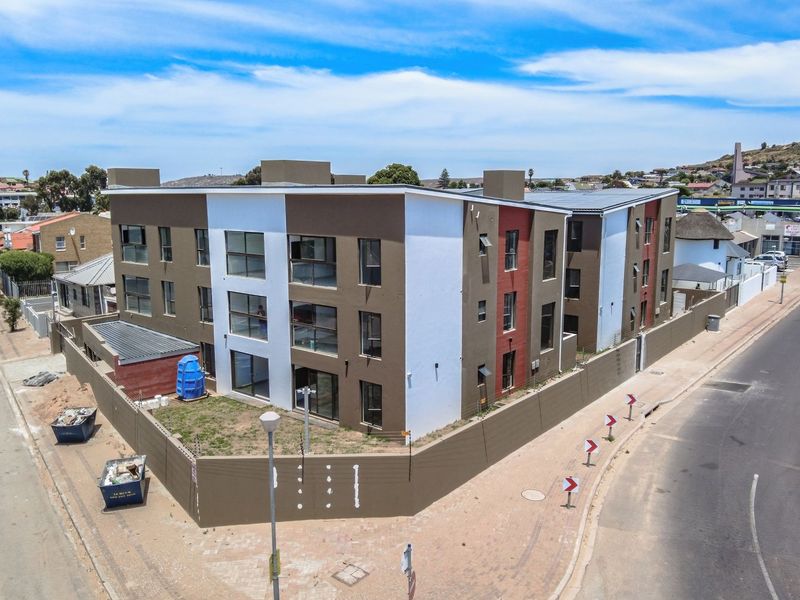 Aerial view of a modern multi-story apartment complex situated on a corner lot with perimeter walling and street access.
