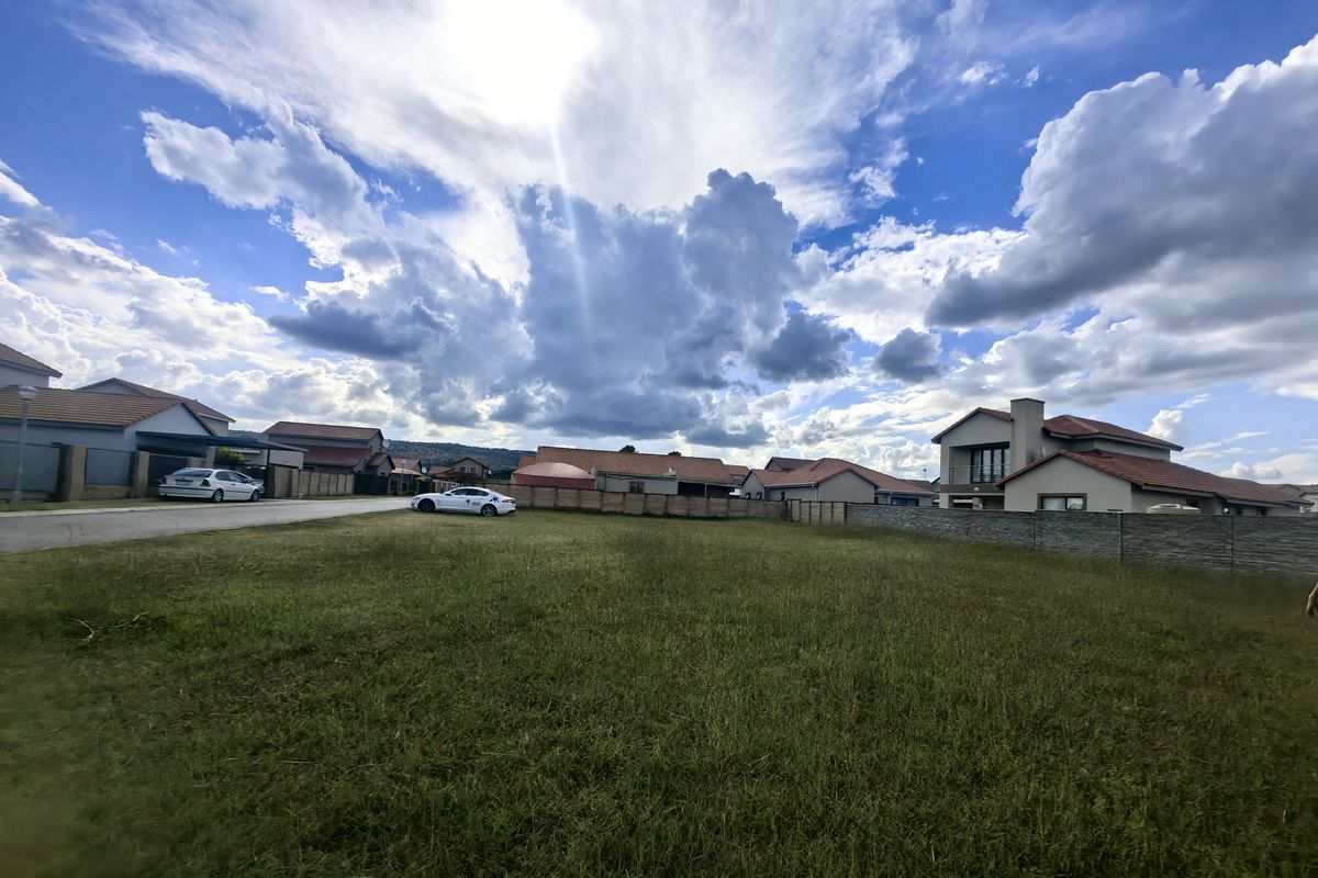 A vacant residential plot featuring a grass lawn and boundary wall, situated within a developed suburban estate.
