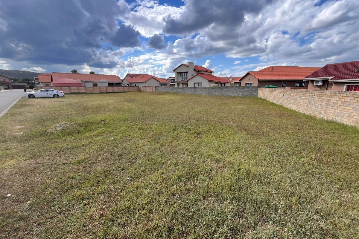 A vacant residential plot of land featuring a grass lawn and enclosed by perimeter brick walls in a suburban neighborhood.
