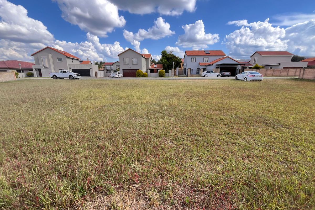 A vacant residential plot of land featuring grass coverage, situated in a developed neighborhood with surrounding residential homes.