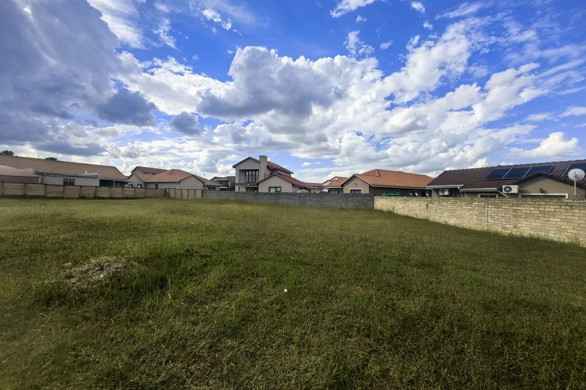 A vacant residential plot featuring a grass lawn and enclosed by perimeter brick walls, situated within an established residential neighborhood.