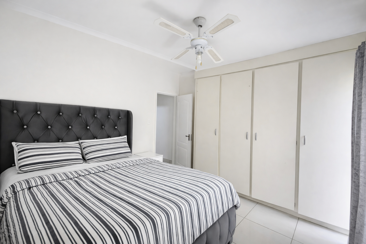 A well-maintained bedroom featuring built-in cupboards, a ceiling fan, and neutral tiled flooring.