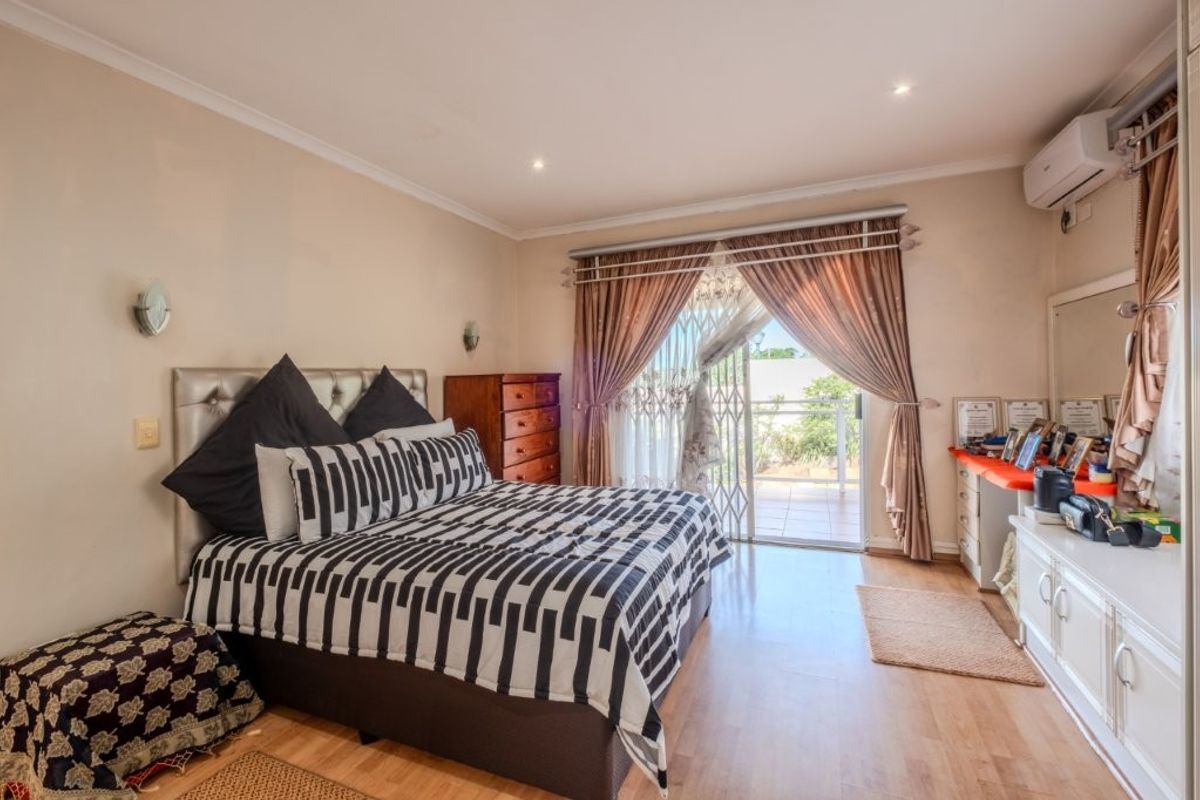 Spacious bedroom featuring laminate flooring, recessed lighting, a wall-mounted air conditioner, and direct access to a private balcony through sliding glass doors.