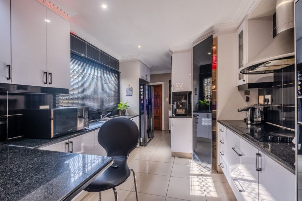 Modern kitchen featuring high-gloss cabinetry, granite countertops, integrated appliances, and sleek tiled flooring with recessed lighting.