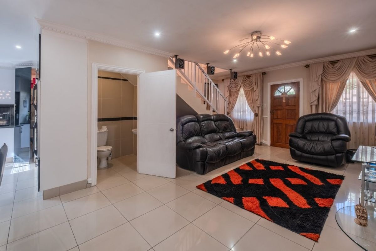 Open-plan living area featuring tiled flooring, a staircase, and an integrated guest toilet, providing a functional layout with direct access to the front entrance.