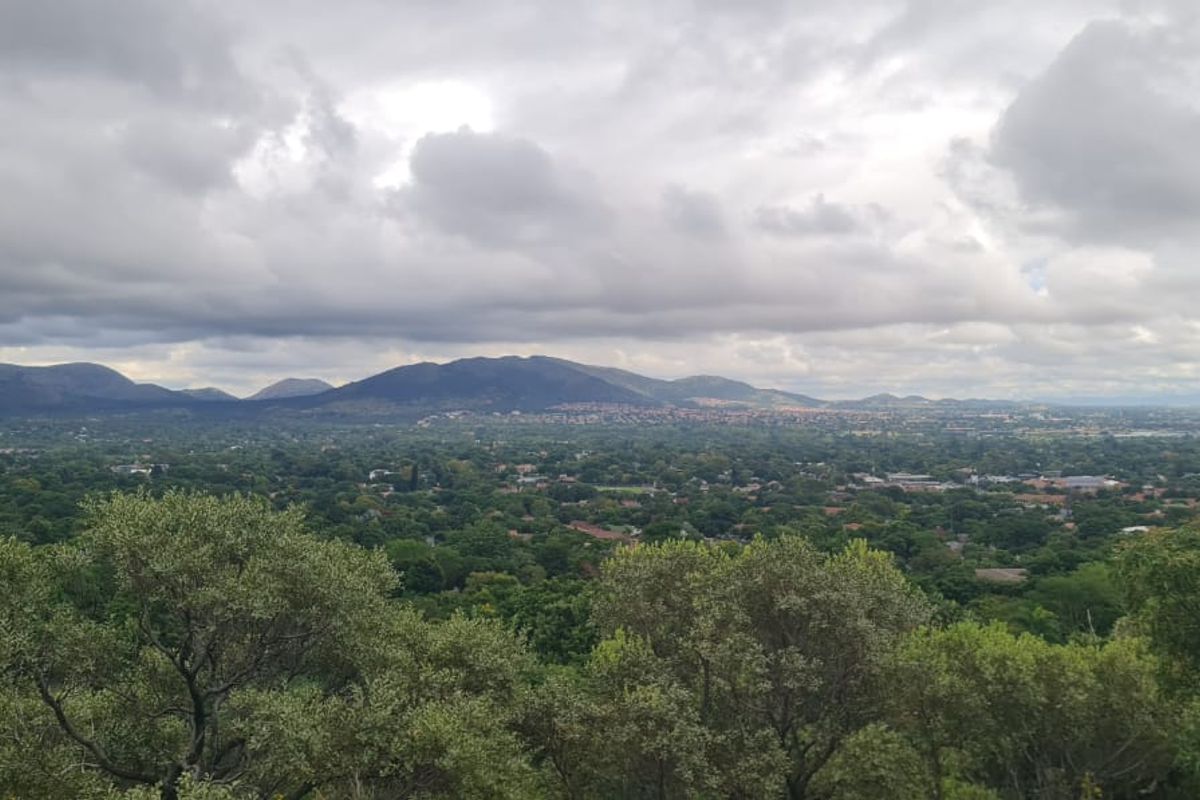 A scenic elevated landscape view overlooking a lush green valley with distant mountains under a cloudy sky.