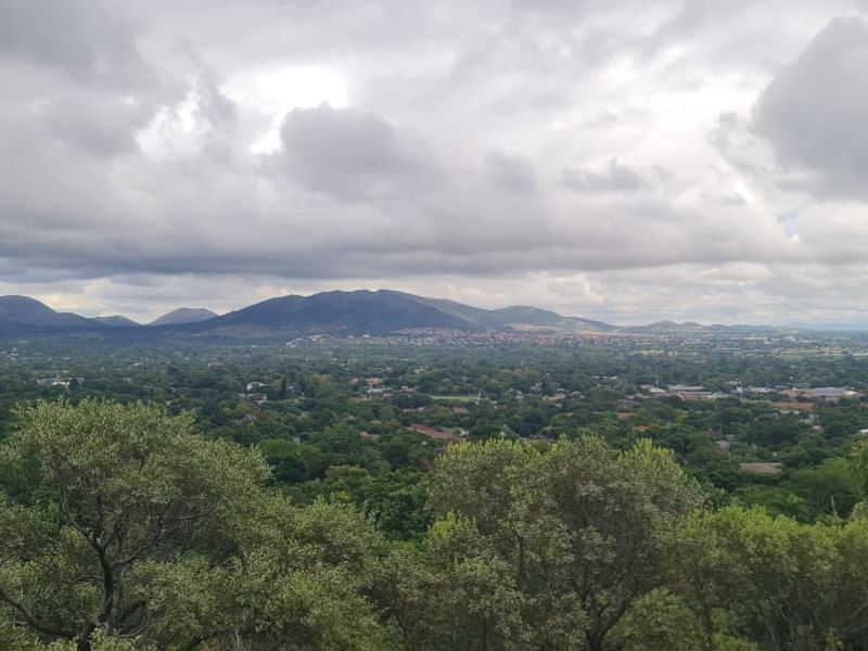A scenic elevated landscape view overlooking a lush green valley with distant mountains under a cloudy sky.