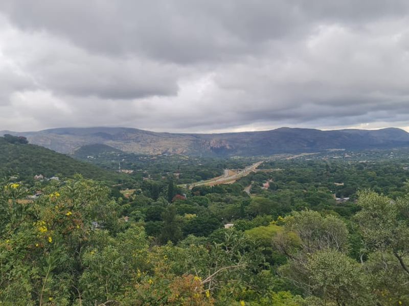 A scenic landscape view overlooking a lush green valley with distant mountains under a cloudy sky.