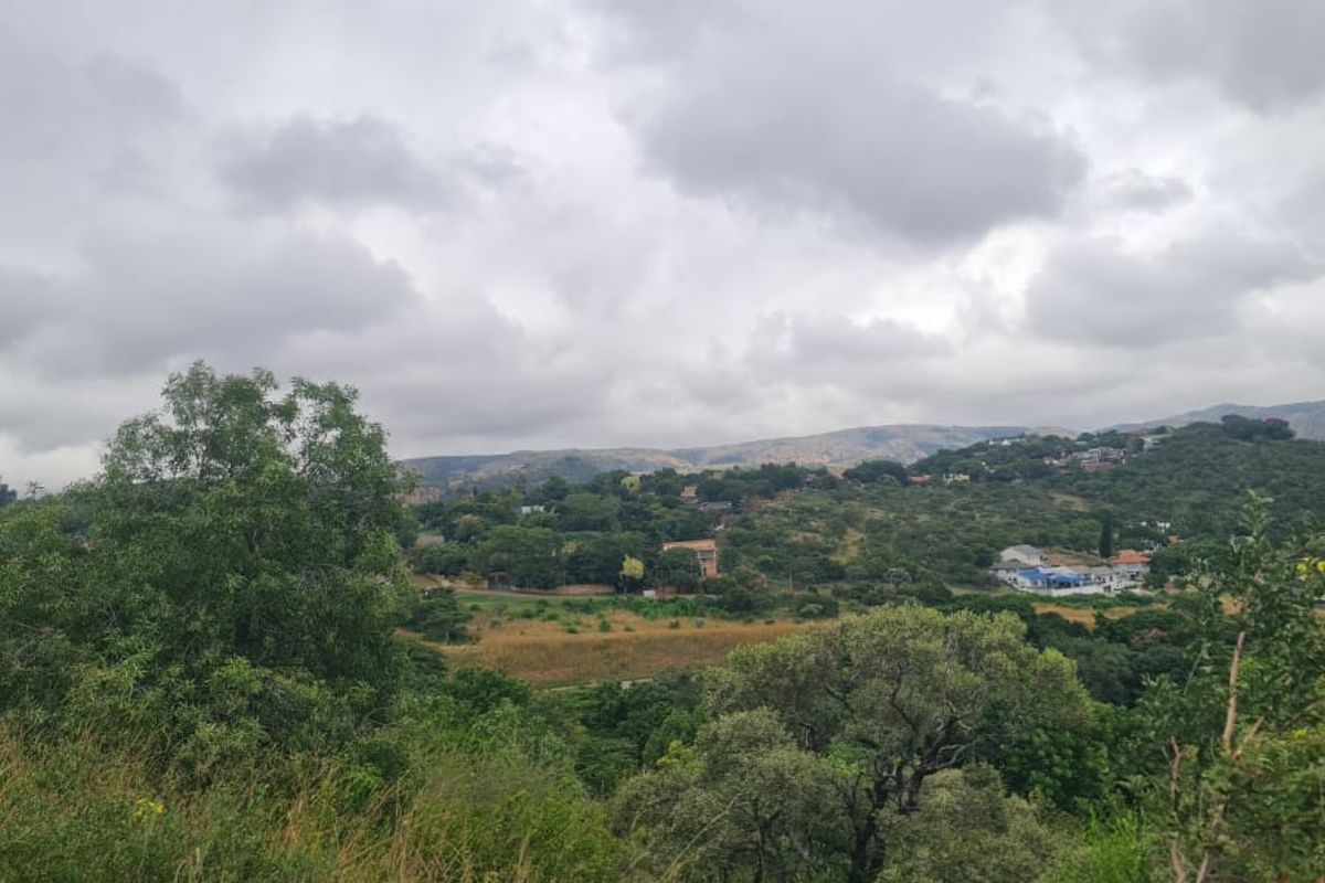 A scenic landscape view overlooking a hilly, vegetated area with distant residential structures under a cloudy sky.