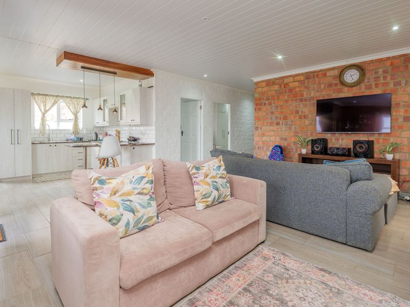 Spacious open-plan living area featuring exposed brick walls, timber-look tile flooring, and a modern kitchen with white cabinetry and a subway tile backsplash.