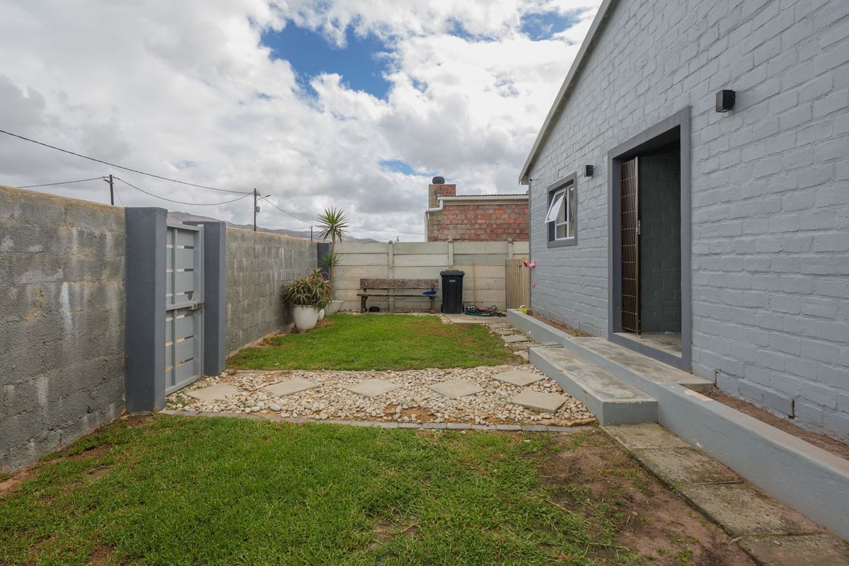 A private rear garden featuring a lawn, stone pathway, and concrete boundary walls, providing a functional outdoor space adjacent to the main dwelling.